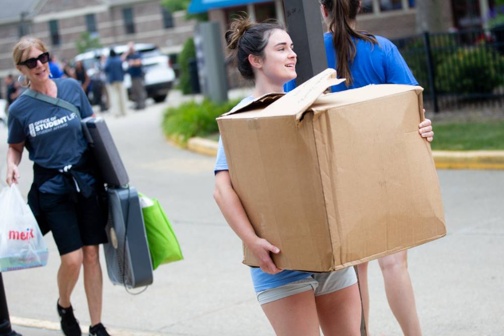An alumna carrying a big box into a dorm.